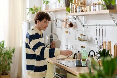 Çizgili tişörtlü genç bir adam evinin keyfini çıkarırken dikkatle bir içki hazırlar..