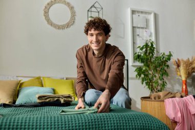 Neşeli genç bir adam rahat bir yatak odasında giysilerini düzenler, huzur dolu bir anın tadını çıkarır..