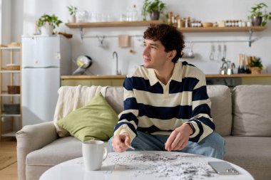 Yakışıklı genç bir adam kanepede oturup sıcak bir evdeki yapbozu tamamlamaya odaklanmış..