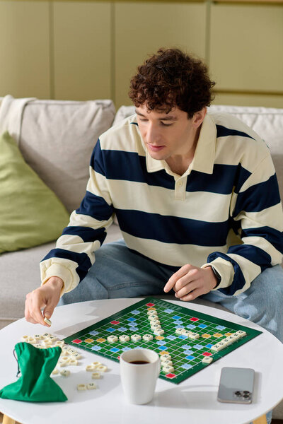 A handsome young man focuses intently on his Scrabble game at home, surrounded by a cozy atmosphere.