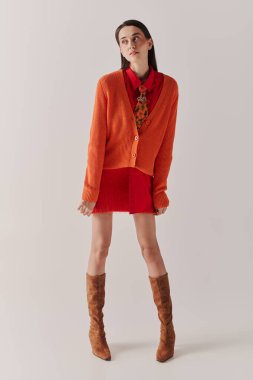 A stunning woman confidently walks in a chic orange and red outfit, radiating style.