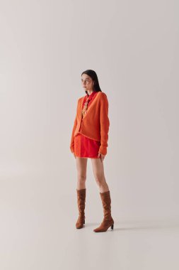 A confident young woman in a bright orange outfit exudes fashionable elegance.