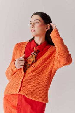 Tarz sahibi genç bir kadın, parlak turuncu giysiler içinde, basit bir arka plana karşı güvenle poz verir..