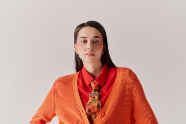 Parlak turuncu hırkalı, kırmızı gömlekli, kendine güvenen genç bir kadın başını çeviriyor..