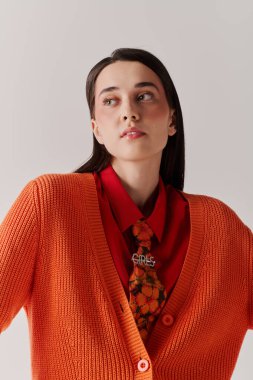 Kendine güvenen bir kadın şık turuncu bir hırka ve kalın kırmızı bir gömlek giyer. Zarif bir şekilde poz verir..