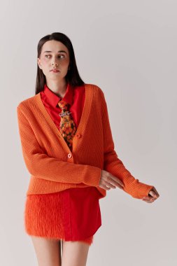 A beautiful woman showcases her unique fashion sense in a stylish orange cardigan and red attire.