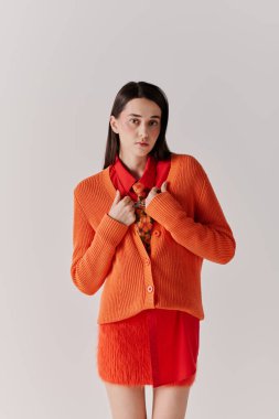 Young woman exudes confidence in a bold orange cardigan and chic red dress, showcasing her style.