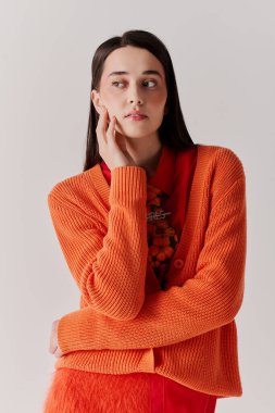 A stylish young woman in a bright orange cardigan displays her fashion sense gracefully.