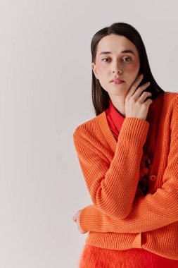 Genç bir kadın zarif turuncu bir kazakla şık yeteneklerini sergileyerek poz veriyor..