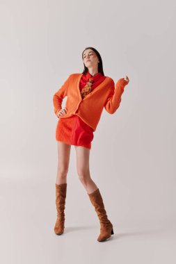 Genç bir kadın dikkat çekici turuncu bir hırka ve şık bir etekle renkli bir elbise sergiliyor..