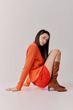 A stylish young woman poses elegantly in a cozy sweater and skirt, radiating confidence and style.