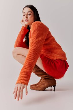 Young woman showcases vibrant fashion with an orange sweater and red skirt, posing artistically.