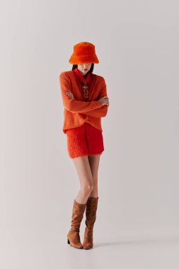 Tarz sahibi genç bir kadın, minimalist bir arkaplanda kendine güvenen eşsiz bir kıyafet sergiliyor..