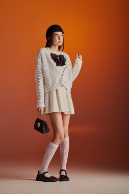 A beautiful young woman showcases her unique style in a trendy outfit against an orange backdrop.