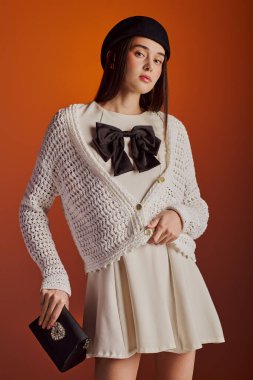 Şık bir kadın zarif bir şekilde poz verir, canlı kıyafetini sıcak bir arkaplanda sergiler..