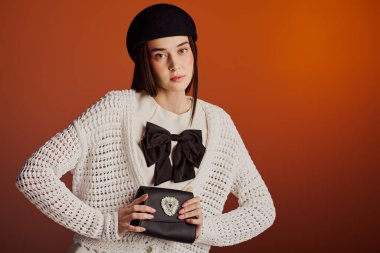 Güzel bir kadın modaya uygun bir kıyafetle poz verir, şık bir debriyaj tutarken cazibe saçar..