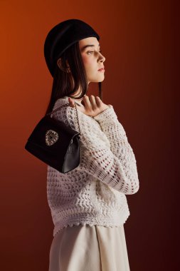 Güzel bir kadın şık bir el çantasıyla rahatça poz verir, rahat örgü bir kazak giyer..