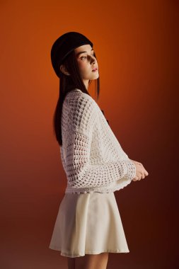 Genç bir kadın zarif, beyaz örgü bir bluz ve neşeli bir etekle poz verir..