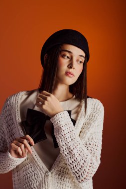 Güzel bir kadın şık kıyafetini sergiliyor ve zarif bir şekilde portakal rengi bir arka plana poz veriyor..