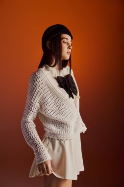 Şık bir kadın zarif bir şekilde turuncu bir arkaplanda poz veriyor, tarzını ve zarafetini sergiliyor..