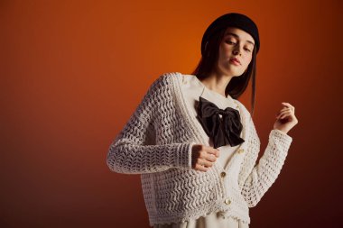 Güzel genç bir kadın şık bir hırka ve şık bir şapka giyer. Kendine güveni ve zarafeti vardır..