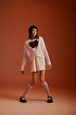 Young woman poses confidently in fashionable attire against a warm backdrop, highlighting her style.