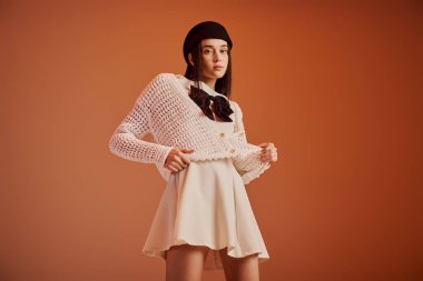 Genç bir kadın, sıcak bir tonla çevrili neşeli bir ifadeyle şık bir moda sergiliyor..