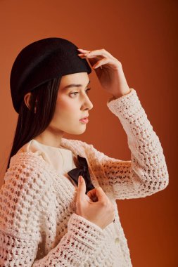 Şık giyinmiş güzel genç bir kadın şık siyah beresini ayarlıyor, kendine güveni tam..