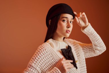 Şık bir genç kadın, şapkasını nazikçe düzeltirken tarzını sergiliyor, kendine güvenini yayıyor..