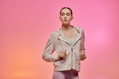 Hareketli giyinen şık genç bir kadın zarif bir şekilde hareket eder, renkli bir arka planla aydınlatılır..