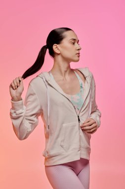 Tarz sahibi genç bir kadın pembe bir arka planda saçlarıyla aktif olarak oynar..