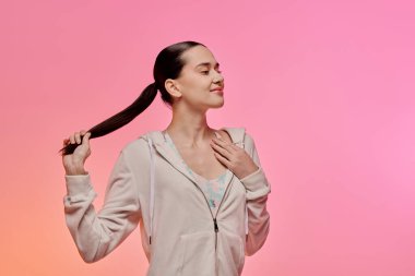 Genç bir kadın nazikçe gülümsüyor, uzun saçlarıyla oynuyor, kendine güveni ve tarzıyla..