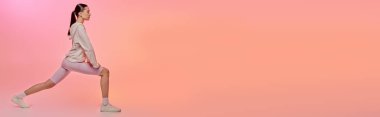 Kendine güvenen spor elbiseli bir kadın yumuşak pembe bir arka plana atlıyor..