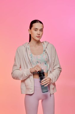 Modayı takip eden genç bir kadın, elinde bir su şişesi, renkli bir zemin üzerinde duruyor..