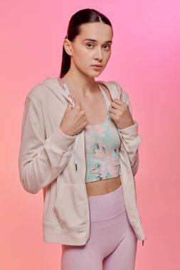 Moda kıyafetli genç bir kadın pembe bir arka plana karşı güven yayıyor..