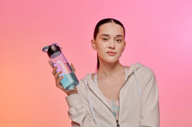 Genç bir kadın renkli bir su şişesiyle su içmeyi teşvik ederken şık bir tarz sergiliyor..