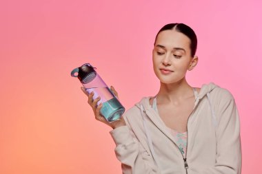 Moda bir su şişesini renkli bir arka planda tutarken şık genç bir kadın gülümsüyor..