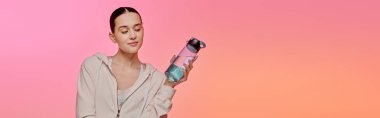Güzel genç bir kadın, renkli bir ortama daldırılmış, modaya uygun bir su şişesi tutuyor..