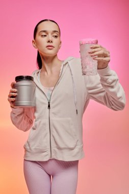 Genç bir kadın zarif bir şekilde canlı bir ortamda protein kabı ve smoothie tutuyor..