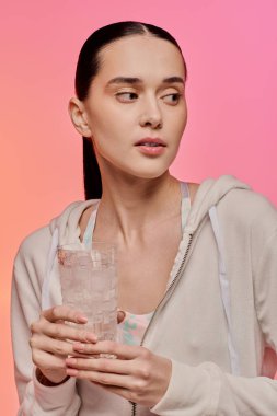 Güzel bir kadın renkli bir ortamda zarifçe poz verirken serin bir bardak su tutar..