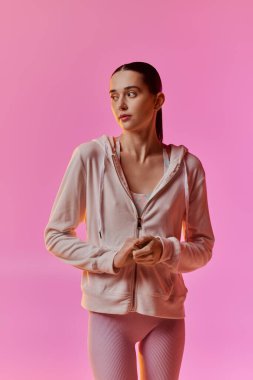 Moda atletizm kıyafetleri içinde güzel bir kadın çarpıcı pembe bir arkaplan önünde rahatça poz veriyor..