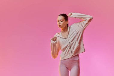 Genç bir kadın neşeyle hareket eder, şık elbisesini canlı pembe bir arka planda sergiler..