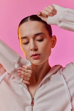 Kendine güvenen bir kadın zarif bir şekilde şık bir elbise içinde parlak pembe bir arkaplan önünde poz verir..