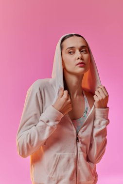 Kapüşonlu eşofmanlı güzel bir kadın çarpıcı pembe bir arka plana zarif bir şekilde poz veriyor..