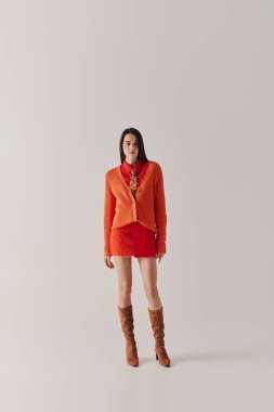 Young woman models a chic orange sweater and red skirt, highlighting her sense of style.