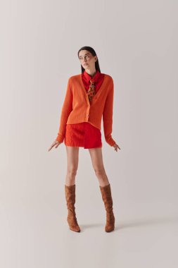 A stunning woman poses confidently in an eye catching orange cardigan and red outfit.