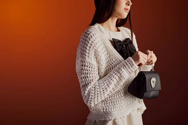 Şık giyinmiş zarif bir kadın sıcak, sanatsal bir arkaplana karşı şık bir el çantası taşıyor..