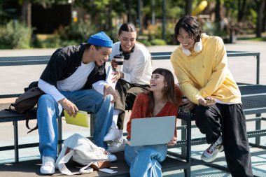 Genç arkadaşlar neşeli bir parkta buluşuyorlar, güneşli bir günde fikir paylaşıyorlar ve gülüyorlar..