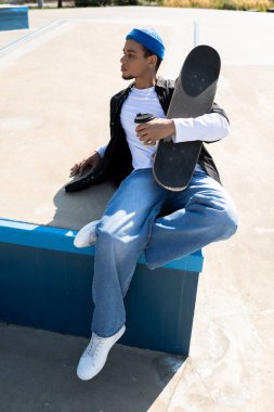 Yakışıklı genç adam kaykay parkında sıradan bir şekilde oturur, kahvesini yudumlar ve dışarıda dinlenir..