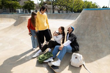 Dört arkadaş bir kaykay parkında toplandı, gülüşlerini ve gülüşlerini açık mavi gökyüzünün altında paylaştılar..